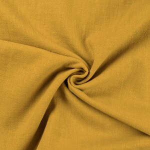 May include: A close-up of a mustard yellow fabric with a textured surface. The fabric is folded and draped, creating a soft and inviting look.