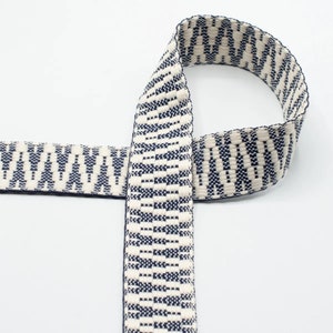 May include: White and navy blue patterned woven webbing. The webbing is approximately 1 inch wide.
