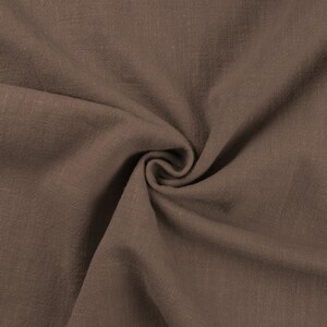 May include: Close-up of a brown fabric with a textured, woven surface. The fabric is folded and draped, showing its soft and drapey texture.