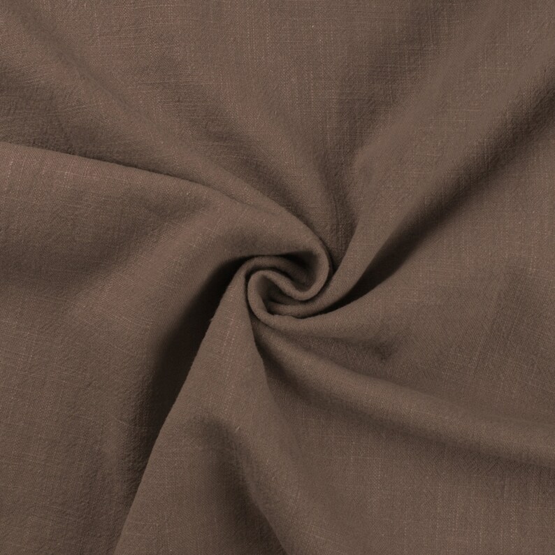 May include: Close-up of a brown fabric with a textured, woven surface. The fabric is folded and draped, showing its soft and drapey texture.
