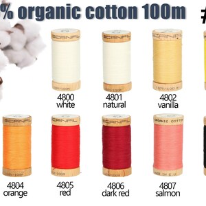 K&ouml;nnte beinhalten: Zehn Holzspulen mit 100% Bio-Baumwollgarn, jede enth&auml;lt 100m Garn. Die Farben umfassen Wei&szlig;, Natur, Vanille, Gelb, Orange, Rot, Dunkelrot, Lachs und Schwarz. Jede Spule ist mit einer Nummer und einem Farbnamen beschriftet.