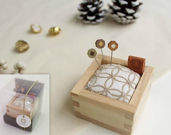 May include: A wooden pin cushion with a white cushion featuring a gold floral design. The cushion is inside a square wooden box. Three decorative pins and a small leather piece are also in the box. The box is in a clear plastic case.