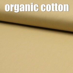 Op de afbeelding: Een close-up van een stuk beige biologisch katoenen stof. De stof is glad en heeft een subtiele glans.