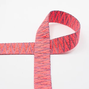 May include: A pink woven ribbon with a textured pattern. The ribbon is folded in half and tied in a knot.