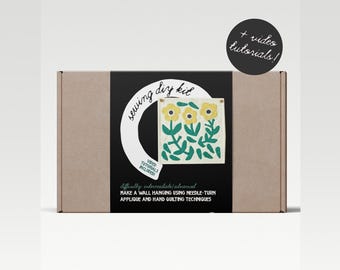 Puede incluir: Una caja de cartón marrón con una etiqueta negra que dice "sewing diy kit" y presenta un diseño floral colorido. La etiqueta también incluye el texto "video tutorials included" y "difficulty: intermediate/advanced". La caja incluye instrucciones para hacer una pared colgante usando la técnica de aplicación de aguja y acolchado a mano.