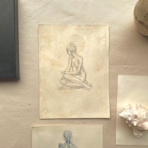 Pode incluir: Um esboço a lápis de uma figura sentada com uma forma de halo acima da cabeça. A obra de arte está em papel envelhecido, rodeada por arte de conchas e uma pintura emoldurada em preto.