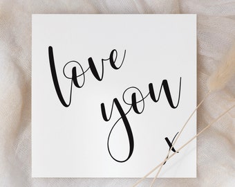 May include: A white card with the words "love you" written in black cursive script. A small "x" is written below the words.