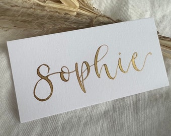 Handgeschreven plaatskaarten met gouden kalligrafie: witte couvert bruiloft