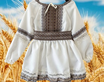 May include: White embroidered dress with brown and black geometric patterns. The dress has long sleeves with lace trim and a lace trim around the bottom hem.