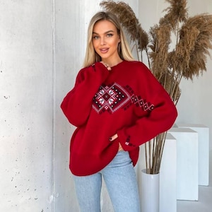 May include: A red knitted sweater with a white and black geometric pattern. The sweater has a relaxed fit and long sleeves.