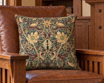 May include: A brown leather armchair with a wooden frame featuring vertical slats. A square throw pillow rests on the seat, displaying a detailed botanical pattern with birds, leaves, and flowers in shades of green, gold, and deep red.
