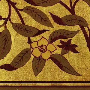 Pu&ograve; includere: Illustrazione botanica con sfondo dorato e design floreale e fogliare. L'immagine mostra un fiore giallo con foglie e rami marroni e verdi. Il design include un bordo marrone scuro nella parte inferiore.