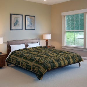 May include: A bed with a dark wooden frame and a green and tan patterned quilt. Two white pillows rest on the bed. Two framed pictures hang on the wall above the bed. A lamp sits on a nightstand.
