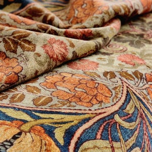May include: A close-up of a fabric with a floral pattern. The fabric is a mix of beige, brown, orange, and blue colours. The pattern features stylised flowers and leaves.