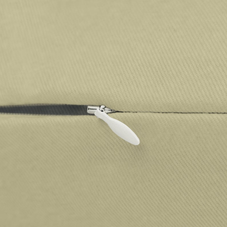 May include: A close-up of a beige pillow with a zipper closure. The zipper pull is white plastic.