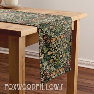 May include: A green, black, orange, and red floral table runner with a repeating pattern. The runner is on a wooden table.