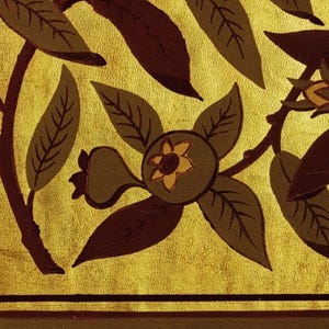 Pu&ograve; includere: Primo piano di un motivo floreale decorativo con foglie e frutti stilizzati nei toni del marrone e verde oliva su sfondo dorato. Il design include un motivo ripetuto di foglie e fiori.