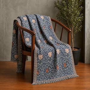 May include: A woven throw blanket featuring a dark blue background with a repeating pattern of light orange and reddish-brown tulips and small white floral accents. The blanket has a textured finish and a fringed edge along the bottom border.