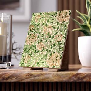 Puede incluir: Un marco de fotos decorativo de madera con un estampado floral. El diseño presenta hojas verdes y flores naranjas sobre un fondo crema. El marco se apoya en un soporte de madera, adecuado para exhibir obras de arte o fotos.
