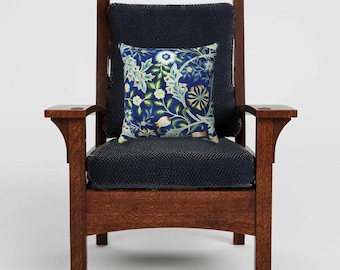 Pode incluir: Uma poltrona de madeira castanho-escura com assento e encosto estofados em tecido azul-marinho texturizado. Uma almofada quadrada está centrada no assento, apresentando um padrão botânico com motivos florais e de folhas em azul, verde, branco e amarelo.
