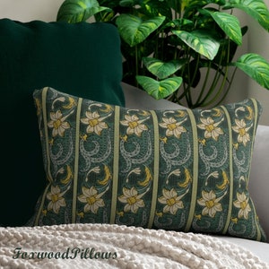 May include: A green and yellow floral patterned cushion with a repeating design of stylised flowers and leaves. The cushion is on a sofa with a white throw.
