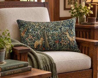 May include: A rectangular throw pillow featuring a woven tapestry design of a forest scene with a fox, a deer, and a bird amidst dense green foliage, dark leaves, and small colorful flowers, set against a neutral-colored upholstered armchair.
