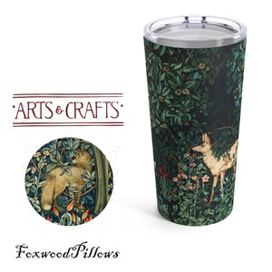May include: A stainless steel tumbler with a green, white, and brown design featuring a fox and a deer in a forest setting. The tumbler has a lid and is printed with the text "Arts & Crafts" and "Foxwood Pillows".