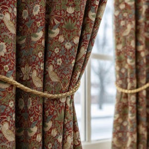May include: Floor-length curtains featuring a dense botanical pattern with birds, flowers, and foliage in shades of deep red, sage green, and muted blue. The fabric is gathered and held back by a thick, twisted gold-colored rope tieback.