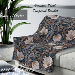 Puede incluir: Una manta de tiro de terciopelo azul y blanco con estampado floral con el texto "Velveteen Plush Pimpernel Blanket" y "William Morris" en la imagen. La manta está colocada sobre un sofá gris claro.