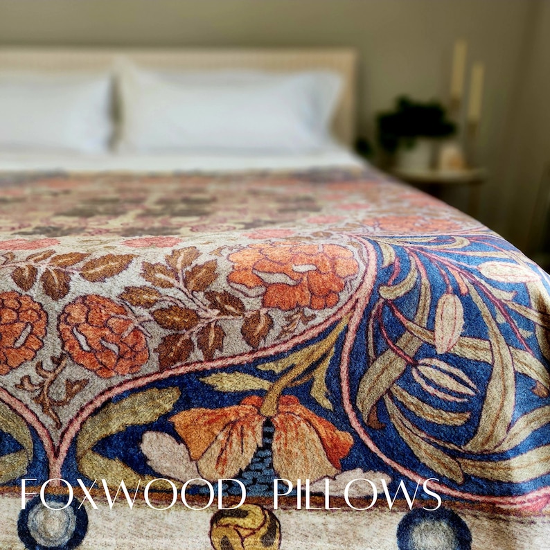 May include: A close-up of a patterned throw blanket with a floral design in shades of blue, orange, and brown. The blanket is on a bed with white pillows and a wooden headboard. The text "FOXWOOD PILLOWS" is visible in the bottom of the image.