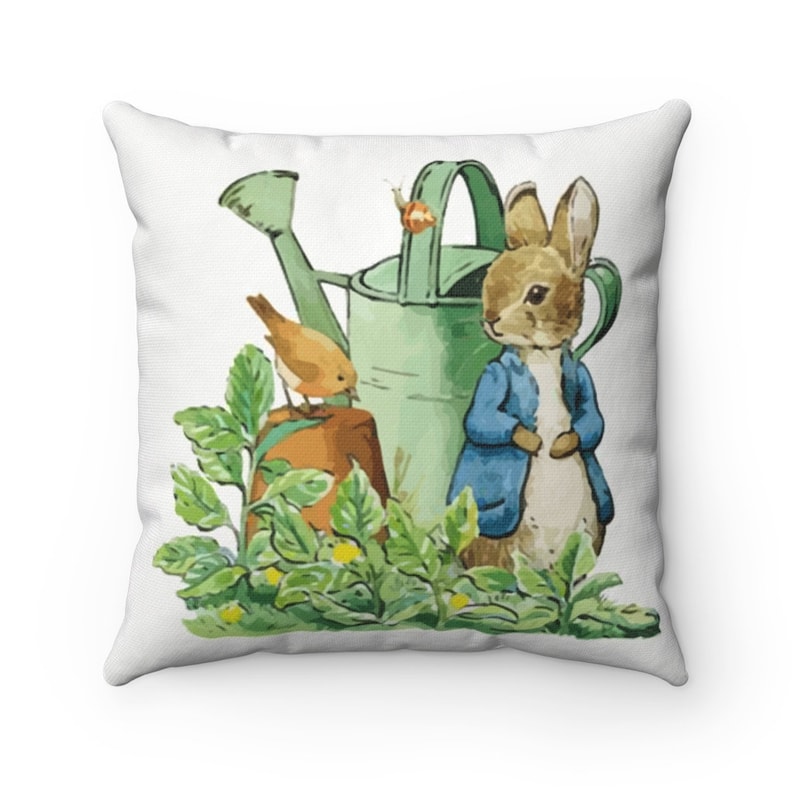 May include: A white throw pillow with a colorful illustration of a rabbit, a bird, and a watering can in a garden setting.