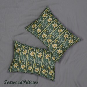 May include: Two green and yellow patterned throw pillows with a floral design. The pillows are arranged on a grey surface.