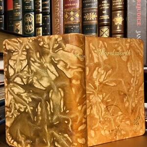 May include: Two leather-bound books with a gold-toned design. The books are titled "Wordsworth" and are sitting on a shelf with other books.