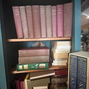 May include: A teal bookshelf filled with vintage books. The top shelf displays a row of maroon-colored books with gold lettering. The middle shelf holds stacked books in various colors, including a green book. The bottom shelf is partially visible, with more books.