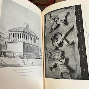 May include: Open book with two black and white illustrations. The left page shows a drawing of a large building with columns, labeled "The Mausoleum of Halicarnassus." The right page displays a relief sculpture.