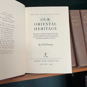 May include: Open book titled "Our Oriental Heritage" by Will Durant, published by Simon and Schuster in 1954. The book is part of "The Story of Civilization" series. The cover is a light beige color.