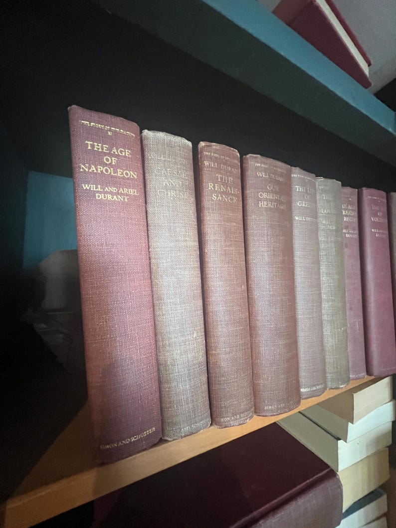 May include: A collection of antique books with maroon and tan covers, arranged on a wooden shelf. The spines display titles like "The Age of Napoleon" and "Caesar and Christ." The books are part of a historical collection.
