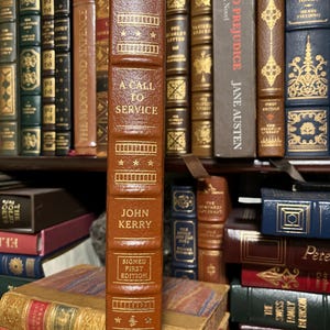 May include: A brown leather-bound book titled "A Call to Service" by John Kerry. The book is a signed first edition.