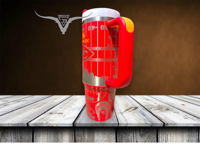 Pu&ograve; includere: Tazza da viaggio in acciaio inox rosso con manico rosso e coperchio bianco. La tazza ha un design con un campo da calcio con un logo di squadra e le parole "City" e "Football".