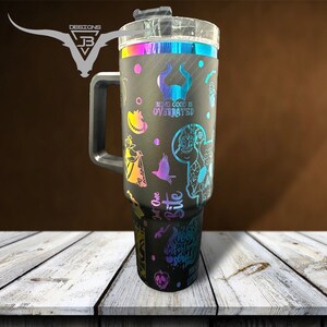 May include: Black stainless steel travel mug with a handle and a clear lid. The mug has a rainbow iridescent finish and features various Disney villain characters and quotes, including "Being good is overrated" and "Just one bite".