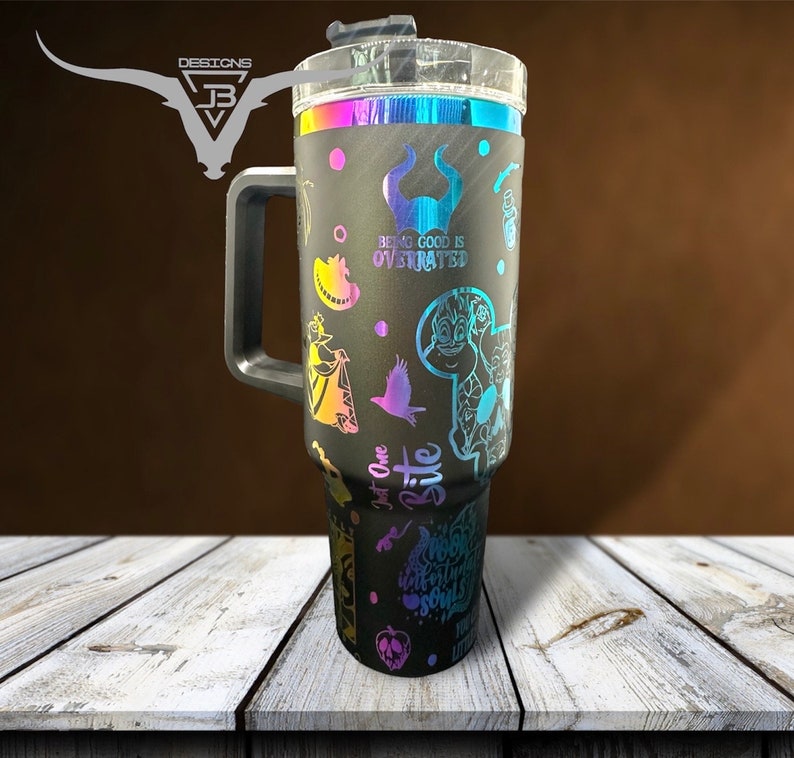 May include: Black stainless steel travel mug with a handle and a clear lid. The mug has a rainbow iridescent finish and features various Disney villain characters and quotes, including "Being good is overrated" and "Just one bite".