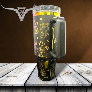 May include: A black stainless steel tumbler with a gold and pink design featuring Disney villains. The tumbler has a black handle and the text "Chillin' Like A Villain" is printed on the side.