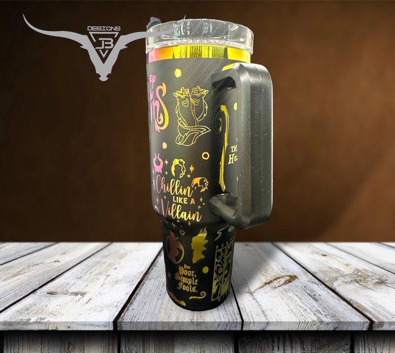May include: A black stainless steel tumbler with a gold and pink design featuring Disney villains. The tumbler has a black handle and the text "Chillin' Like A Villain" is printed on the side.