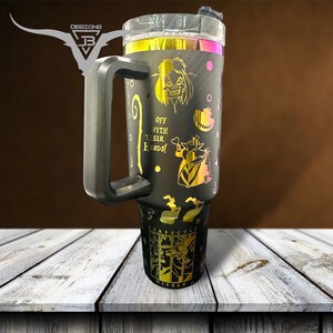 May include: Black stainless steel tumbler with a gold glitter finish and a black handle. The tumbler features a design of characters from the movie "Wicked" with the text "Off with their heads!" and "Perfectly Wicked".