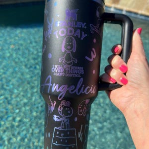 May include: Black stainless steel travel mug with a purple and white design featuring a cartoon dog. The mug has a black handle and the text "Stanley. Today. I will not stress over things I can't control. Angelica" is printed on the side.
