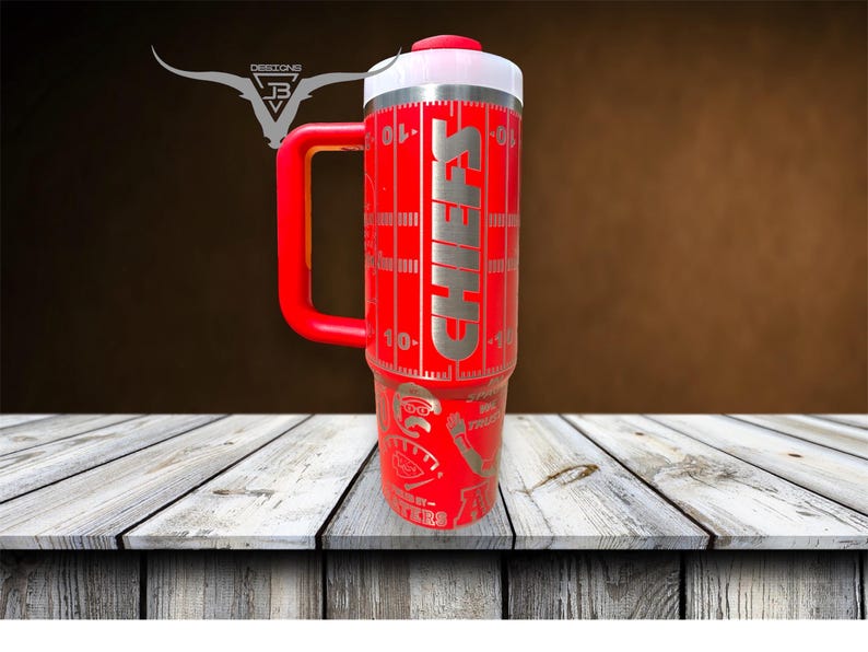 Pu&ograve; includere: Tazza da viaggio in acciaio inox rosso con manico nero e coperchio bianco. La tazza ha un design da campo da calcio con la scritta "CHIEFS" stampata su di essa.