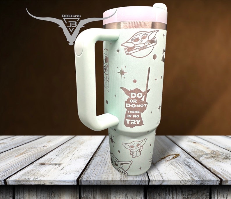 Puede incluir: Un vaso de acero inoxidable verde claro con tapa y asa blancas. El vaso presenta un patr&oacute;n repetido de un personaje de dibujos animados con el texto "Do or Do Not, There is No Try".