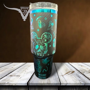 May include: A black and teal tumbler with a design featuring various Disney villains, including Ursula, Maleficent, and Cruella de Vil. The text "You Clumsy Little Fool!" is printed on the bottom of the tumbler.