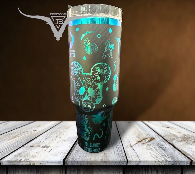 May include: A black and teal tumbler with a design featuring various Disney villains, including Ursula, Maleficent, and Cruella de Vil. The text "You Clumsy Little Fool!" is printed on the bottom of the tumbler.