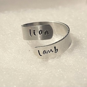 Puede incluir: Un anillo de plata con las palabras "león" y "cordero" grabadas.
